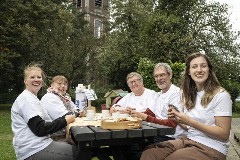 Vijf vrijwilligers in wit T-shirt zitten aan de picknicktafel in de inclusieve tuin De Nestel in Grembergen.
