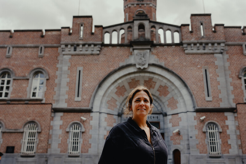 Marlies Gailliaert van vzw De Huizen poseert voor de ingang van een gevangenis.