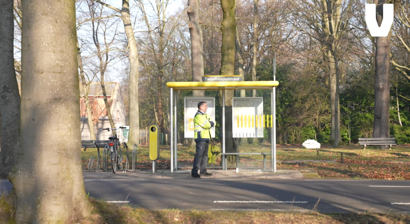 Lijncontroleur staat te wachten aan bushokje.