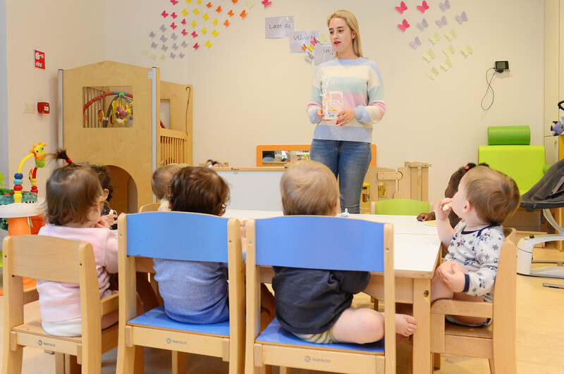 Jonge peuters kijken en luisteren al zittend op stoeltjes naar de kinderbegeleidster
