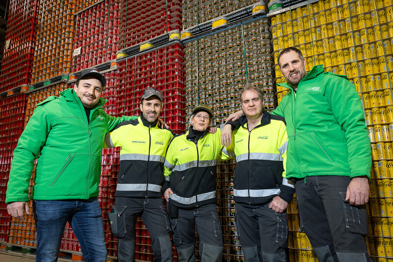 Vijf ACV-militanten poseren voor verschillende palletten frisdrank in de Coca-Cola-fabriek te Zwijnaarde.