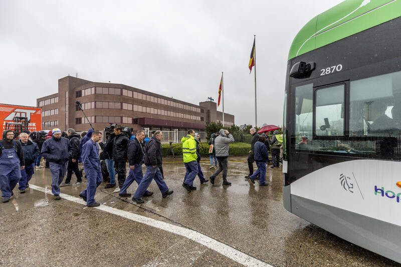 Arbeiders na de ondernemingsraad op het bedrijfsterrein van Van Hool met een bus op de voorgrond