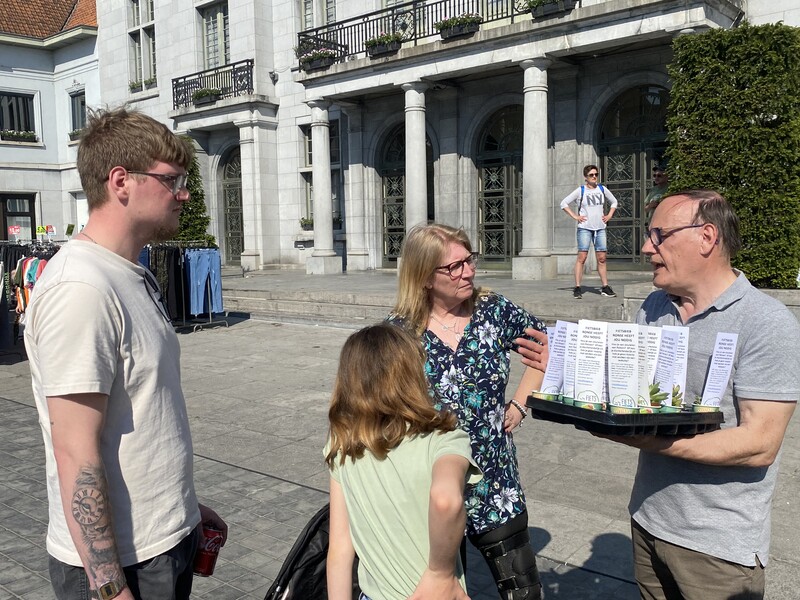 Een man deelt een vetplantje uit aan een jong gezin en geeft uitleg over het project 'Fietsbieb'.