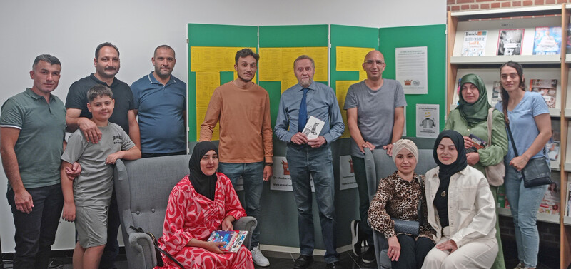 Een groep mensen met migratieachtergrond poseren samen met de leerkracht tijdens de Nederlandse les.