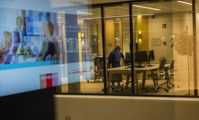 Kijk van buiten binnenin kantoorgebouw waar vrouw schoonmaakt