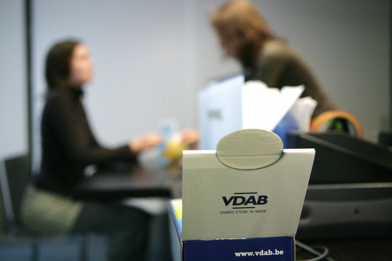 logo van VDAB op voorgrong, met wazig op achtergrond een werkzoekende en haar VDAB-coach