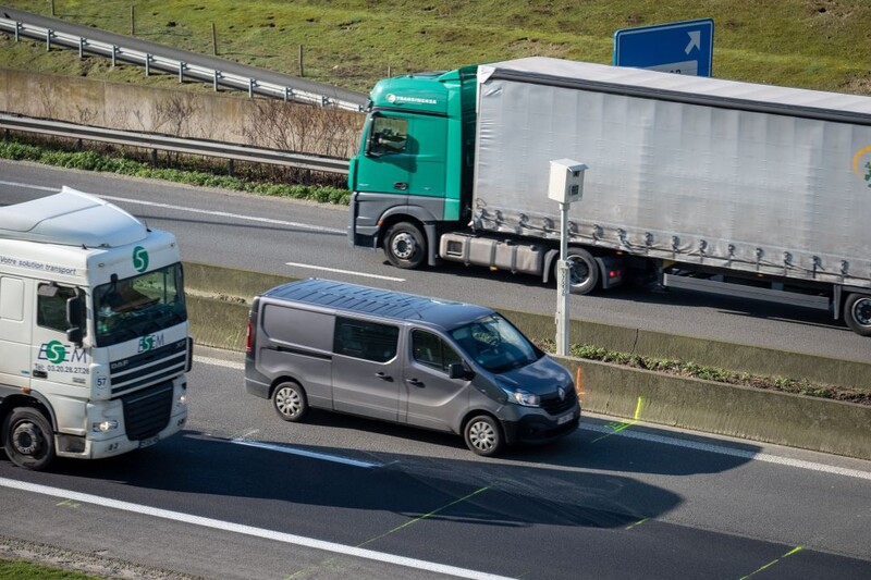 Een bestelwagen en vrachtwagens rijden voorbij een flitspaal op de snelweg.