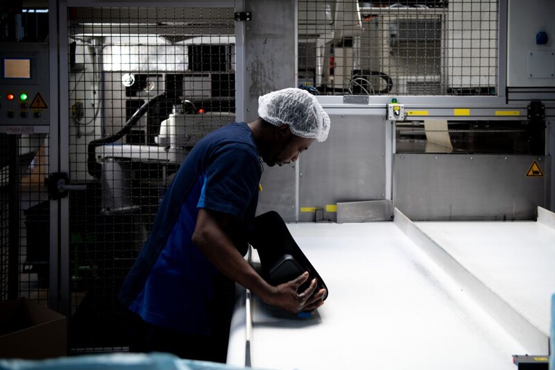 Een zwarte werknemer in blauwe overall en hoofdkapje is aan het werk in een fabriek.