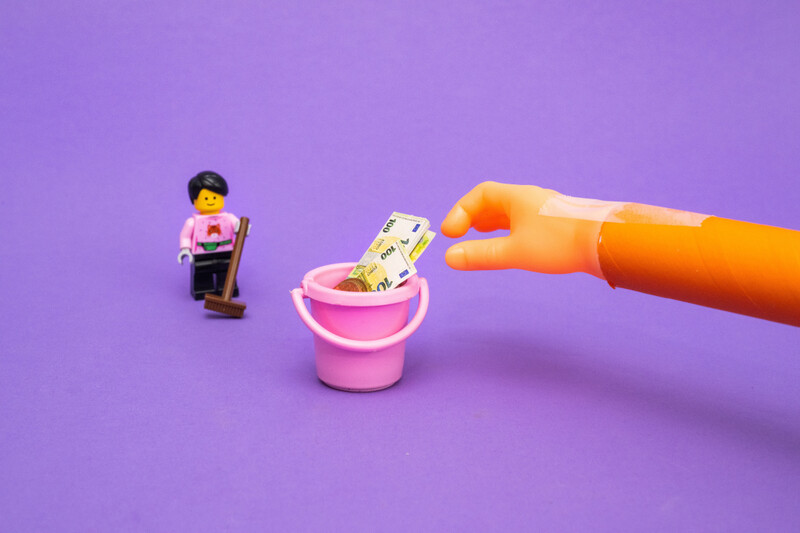 Hand steelt geld uit emmer van huishoudhulp, illustratieve voorstelling uit LEGO en ander speelgoed