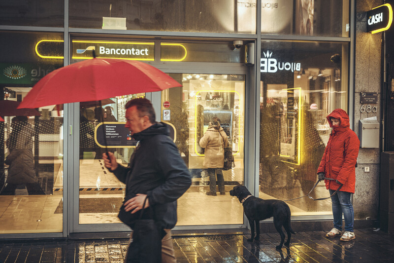 Bancontact geldautomaat in de Kapellestraat Oostende. Regen en man met paraplu wandelt door beeld