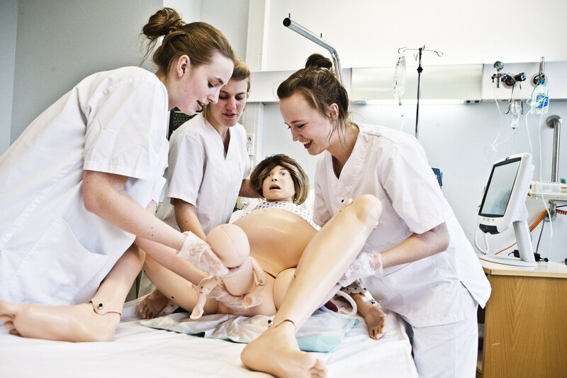 Drie vroedvrouwen in opleiding oefenen een bevalling op een pop
