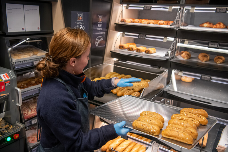Jonge jobstudent vult vers afgebakken broodjes aan in de supermarkt