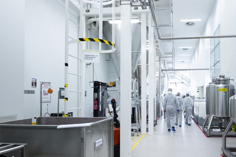 Groep mensen in beschermende, witte pakken wandelen door de productieruimte van Janssen Pharmaceutical