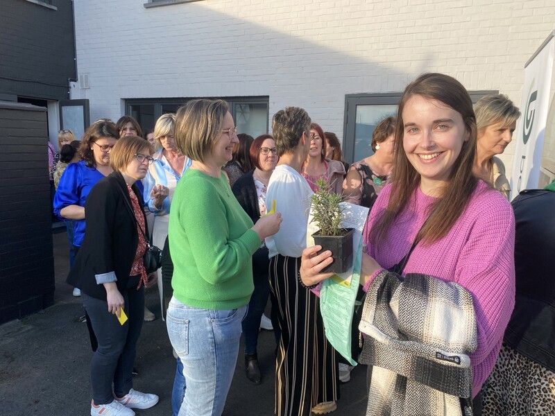 Een Familiehulp-personeelslid poseert met een lavendelplantje in de hand voor een rij wachtenden.