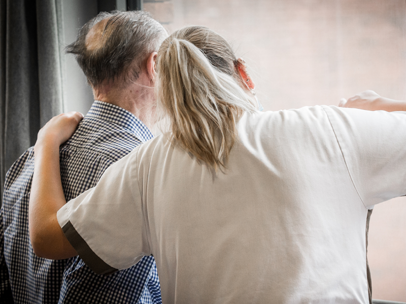 Verpleegster en rusthuisbewoner kijken samen uit het raam