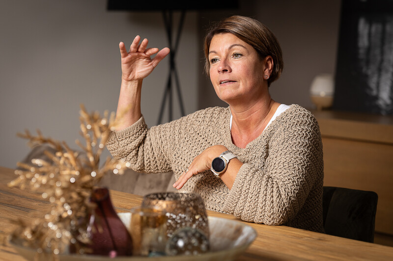Ann zit aan tafel en maakt met haar handen een gebaar tijdens het gesprek over opgroeien in een gewelddadig gezin.
