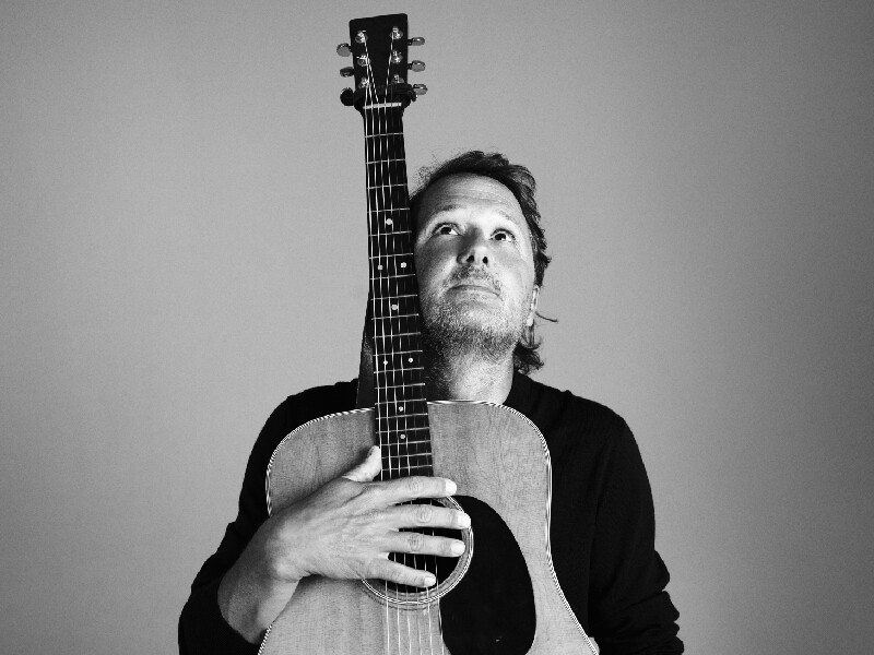 Joost zwegers staat met gitaar in zwart wit foto